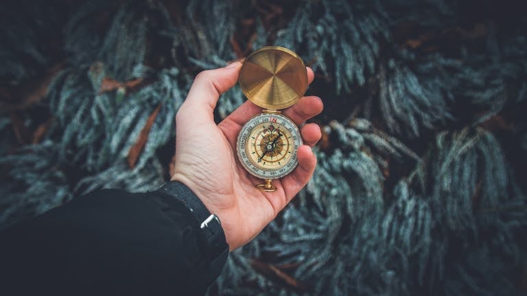 A close-up shot of a hand holding a vintage compass against a natural background.